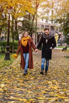 In love couple walking in the autumn park holding hands. Outdoor shot of a young couple in love walking along a path through a autumn park. Tinted image. 