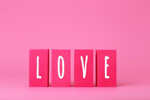 Word love written on pink toy blocks against pink background with copy space. Concept of Valentine's day, self love, romance, dating or anniversary