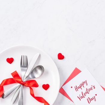 Valentine's Day holiday dating meal, banquet greeting card design concept - White plate and red ribbon on marble background, top view, flat lay.