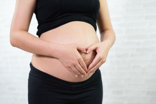 Pregnant woman holding her hands in a heart shape on her belly.