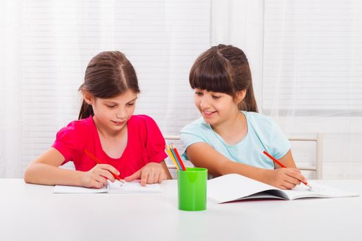 Two concentrated schoolgirls drawing at table