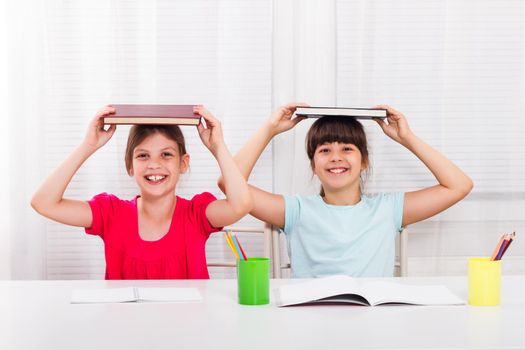 Two happy schoolgirls with books at table looking into camera