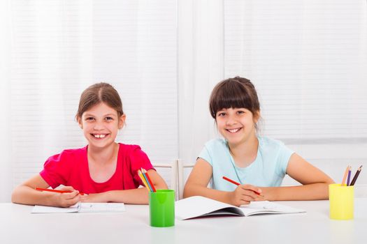Two happy schoolgirls drawing at table