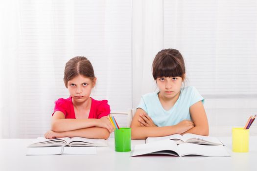Two little angry schoolgirls sitting at tale
