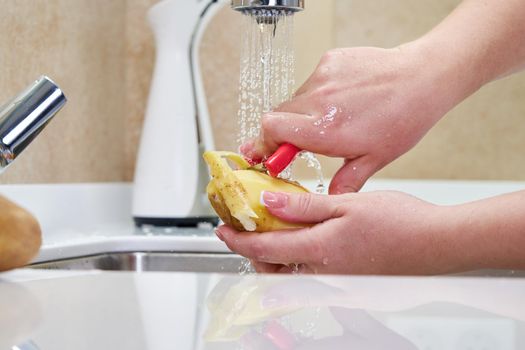 Woman housewife peels potatoes with a knife in the sink over the sink.