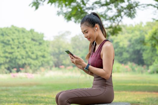 Beautiful Asian woman enjoy to use mobile phone with relaxation after exercise in park or garden.