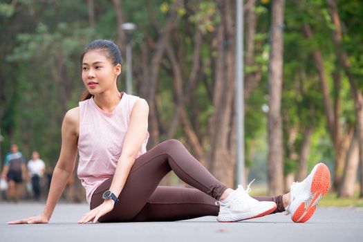 Asian sport woman sit and stretching body and leg on road of park or garden in the morning.