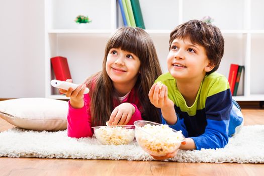 Image of children eating popcorn and watching tv at home.