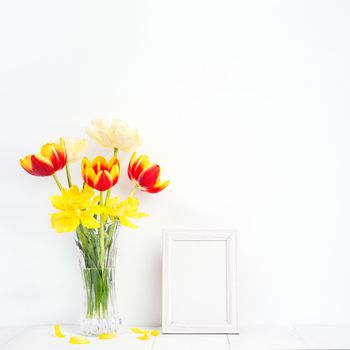 Tulip flower in glass vase with picture frame place on white wooden table background against clean wall at home, close up, Mother's Day decor concept.