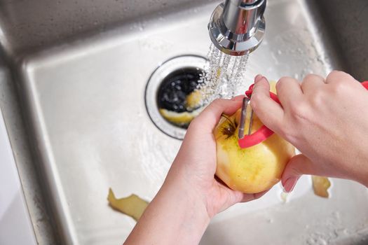 Cropped view of female hands peeling apple over Food waste disposer machine in modern kitchen
