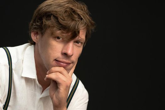 Thoughtful handsome young fluffy hair hipster man sitting leaned head on his hand isolated on black background. Copy space on the right.