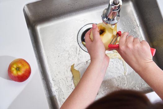 Cropped view of female hands peeling apple over Food waste disposer machine in modern kitchen