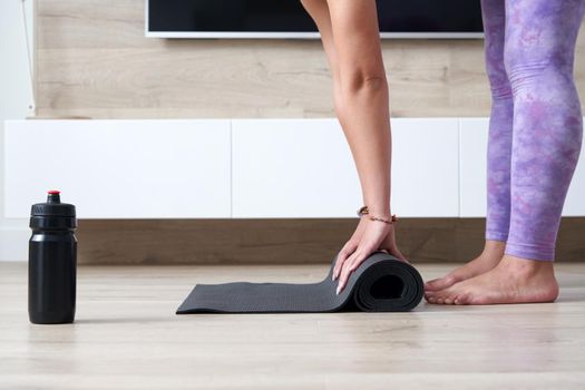 young woman folding black yoga or fitness mat after working out at home in living room