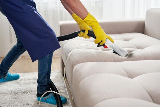 Dry cleaning worker removing dirt from sofa indoors