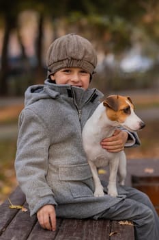 Caucasian boy sits on a bench with a dog Jack Russell Terrier for a walk in the autumn park