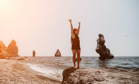 Woman travel sea. Young Happy woman in a long red dress posing on a beach near the sea on background of volcanic rocks, like in Iceland, sharing travel adventure journey