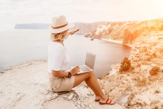 Digital nomad, Business woman working on laptop by the sea. Pretty lady typing on computer by the sea at sunset, makes a business transaction online from a distance. Freelance remote work on vacation