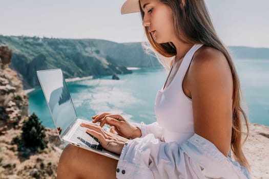 Digital nomad, Business woman working on laptop by the sea. Pretty lady typing on computer by the sea at sunset, makes a business transaction online from a distance. Freelance remote work on vacation