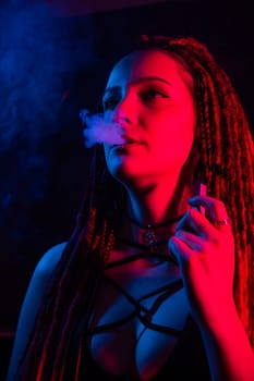 Caucasian girl with dreadlocks smokes a vape in red blue light