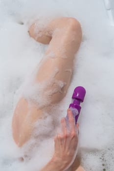 A woman lies in a bubble bath and holds a purple vibrator