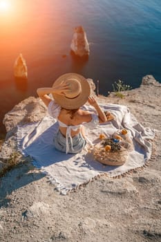 woman sea travel. photo of a beautiful woman with long blond hair in a pink shirt and denim shorts and a hat having a picnic on a hill overlooking the sea.