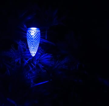 Blue light bulb shaped as a pinecone among the pine leaves in the night dark.
