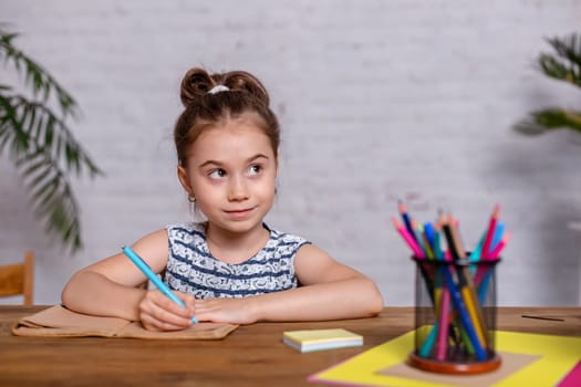 Inspired little girl at the table draw with crayons or do home work. Studying in elementary school. Home education