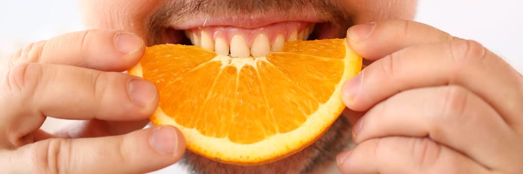 Portrait of smiling man with slice of juicy orange. Vitamins antioxidants in citrus fruits