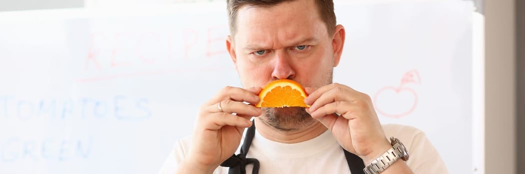 Angry sad male cook with orange slice frown. Negative emotions stress and depression in kitchen