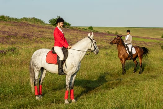 Horseback riders. Two attractive women ride horses on a green meadow. Horse riding. Horse racing. Rider on a horse.