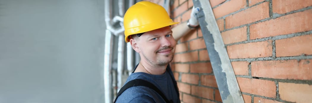 Male builder mason makes brickwork of walls and holds working tool. Construction services concept