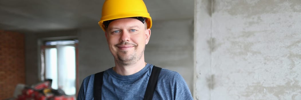 Joyful handyman, builder in uniform and hard hat looks at camera and takes notes on clipboard. Builder foreman preparing for repair work