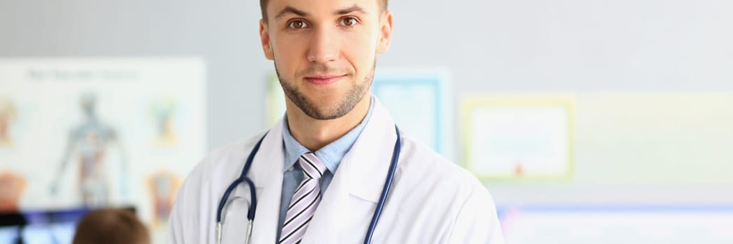 Portrait of smiling young doctor with a stethoscope on background of office in clinic. Medical services and insurance