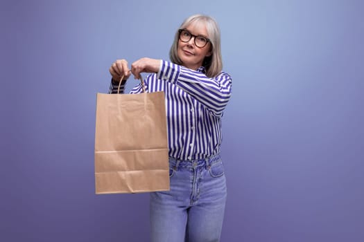 fashionable middle-aged woman with gray hair holding out a package with social assistance on a bright studio background with copy space.