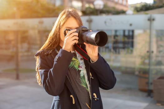 Portrait of professional female photographer on the street photographing on a camera. Photo shoot photosession in the city