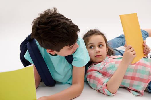 Authentic portrait of school kids, a little girl and teen boy looking at each other, holding textbooks and school supplies, isolated on white studio background. Back to school Education Study Learning