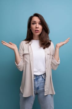 surprised 30s brunette woman dressed in a shirt throws up her hands.