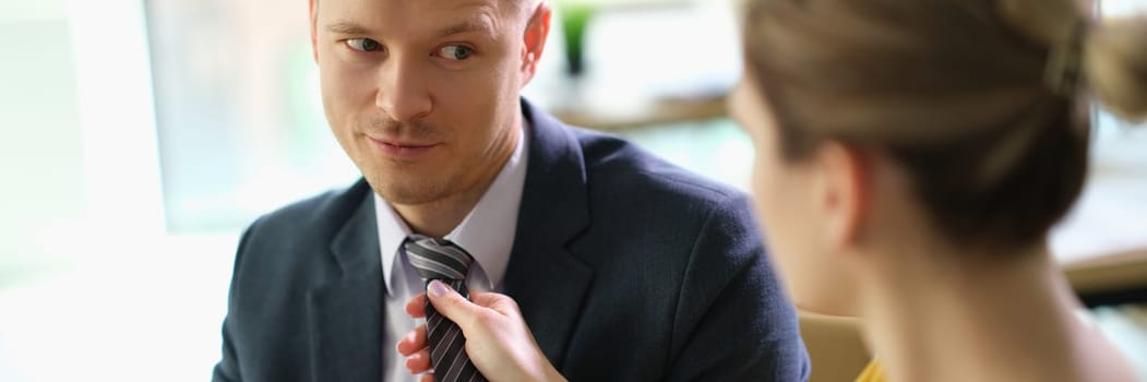 Woman secretary straightening tie to manager man at work in office. Romantic relationship at work career growth concept