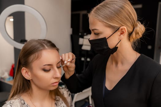 Makeup artist paints eyelashes to a woman in a beauty salon