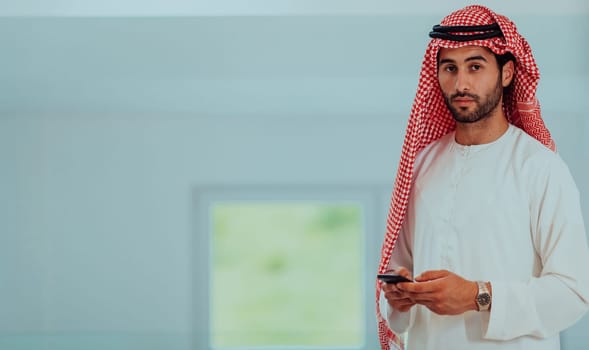 Young modern Muslim Arabian businessmen wearing traditional clothes while using smartphones at home