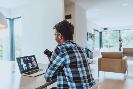 The man sitting at a table in a modern living room, using a smartphone and laptop for business video chat, conversation with friends and entertainment.