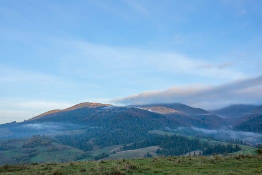 Early morning in summer Ukrainian Carpathians. Clouds over mountains and light fog between wooded hills