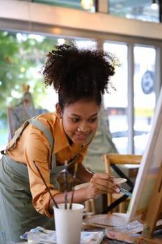 Talented African American female artist painting on canvas in art workshop. Art, creative hobby and leisure activity concept.