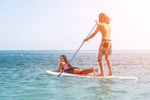 Silhouette of woman standing, surfing on SUP board, confident paddling through water surface. Idyllic sunset or sunrise. Sports active lifestyle at sea or river.