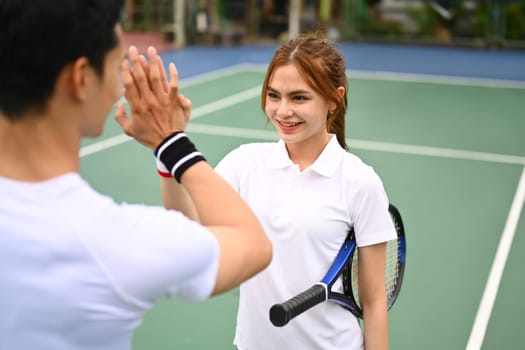 Cheerful young female tennis player giving high five with competitor at tennis court after the match.