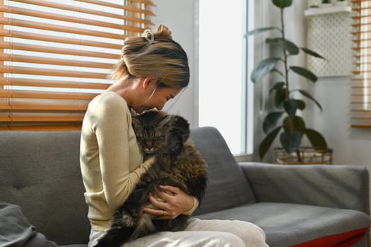 Loving young woman playing with her fluffy cat at home. Human, domestic pet and lifestyle concept.