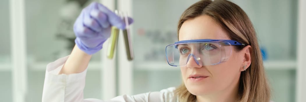 Woman chemist in protective glasses holding test tubes with liquid in hands in laboratory. Pharmaceutical business concept