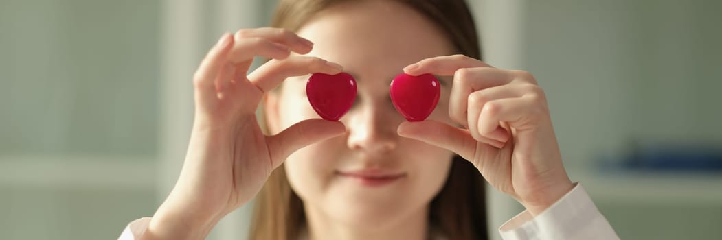 Doctor cardiologist holding two toy red hearts in front of eyes closeup. Cardiology medical care concept