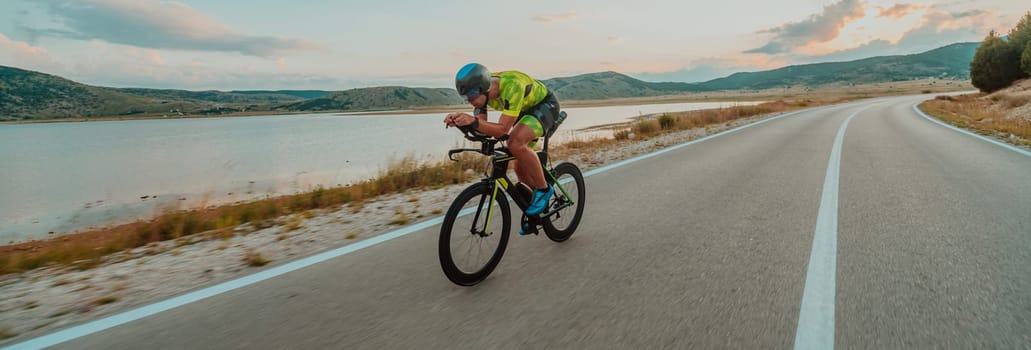 Full length portrait of an active triathlete in sportswear and with a protective helmet riding a bicycle. Selective focus.