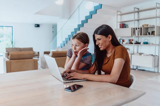 Mother with her daughter talking on laptop with family and friends while sitting in modern living room of big house.